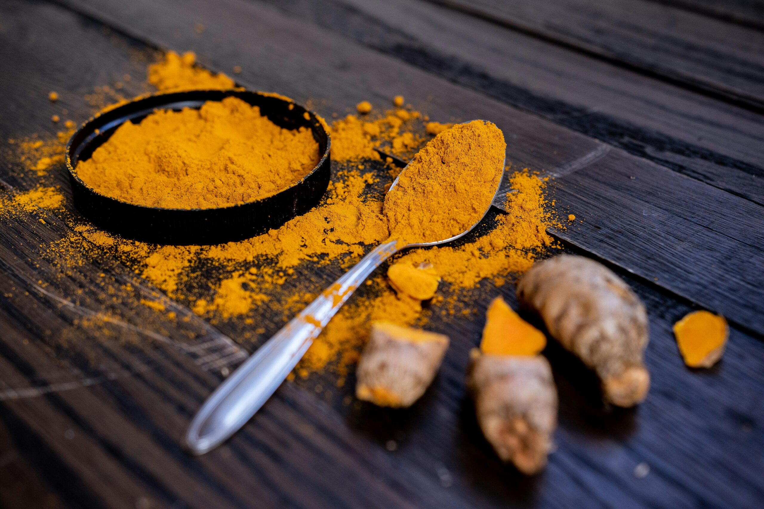 Vibrant turmeric powder and root on a dark wooden surface, emphasizing natural spices. 10 serious side effects of turmeric
